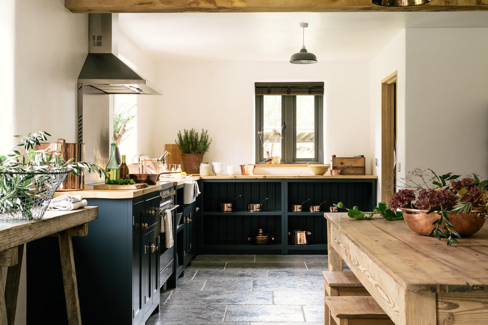 Photo of a medium sized rural l-shaped kitchen/diner in Other with a belfast sink, shaker cabinets, blue cabinets, wood worktops, stainless steel appliances, limestone flooring and no island.
