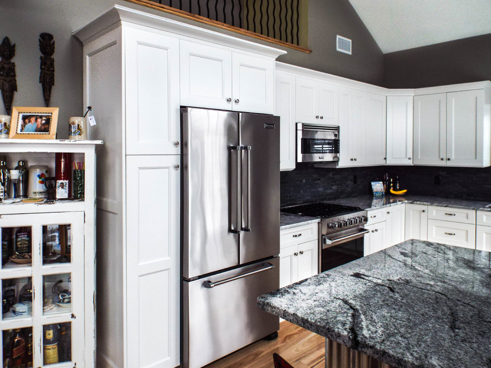 Photo of a large urban l-shaped kitchen/diner in New York with a built-in sink, recessed-panel cabinets, white cabinets, granite worktops, grey splashback, stone tiled splashback, stainless steel appliances, light hardwood flooring and a breakfast bar.