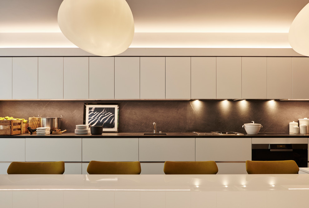 Photo of a large contemporary l-shaped open plan kitchen in London with an integrated sink, flat-panel cabinets, white cabinets, black appliances and multiple islands.