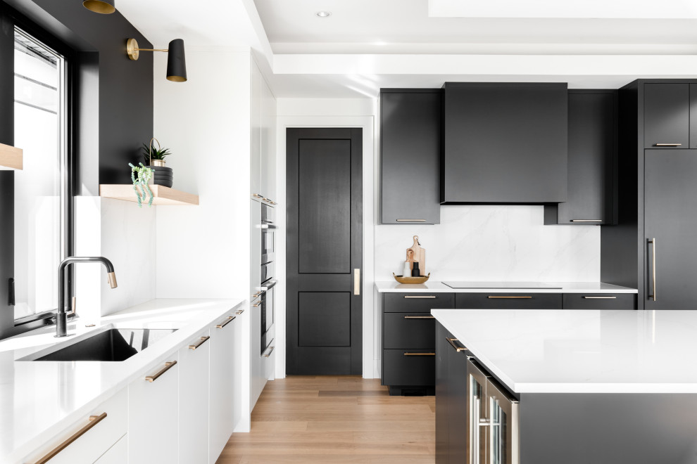 Modern inredning av ett vit vitt l-kök, med en undermonterad diskho, släta luckor, svarta skåp, bänkskiva i kvarts, vitt stänkskydd, integrerade vitvaror, ljust trägolv, en köksö och beiget golv