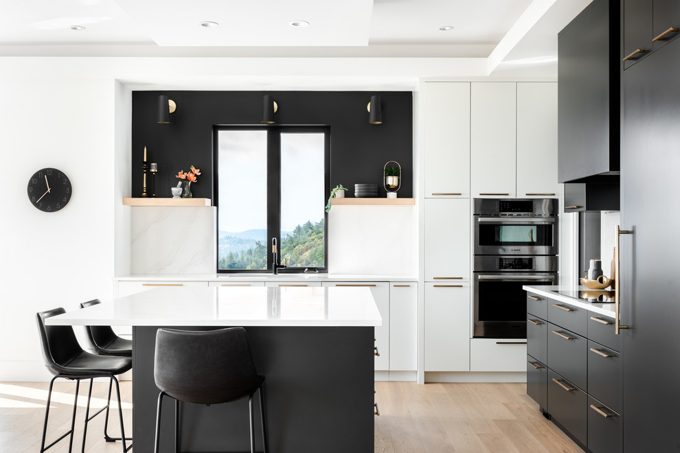 Foto di un cucina con isola centrale design con ante lisce, ante nere, paraspruzzi a finestra, elettrodomestici in acciaio inossidabile, parquet chiaro, pavimento beige e top bianco