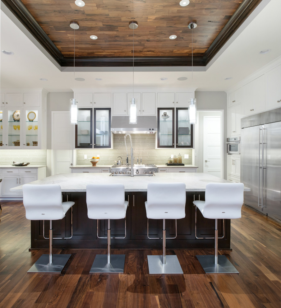 カンザスシティにあるトランジショナルスタイルのおしゃれなキッチン (エプロンフロントシンク、シェーカースタイル扉のキャビネット、白いキャビネット、グレーのキッチンパネル、シルバーの調理設備、無垢フローリング、茶色い床) の写真
