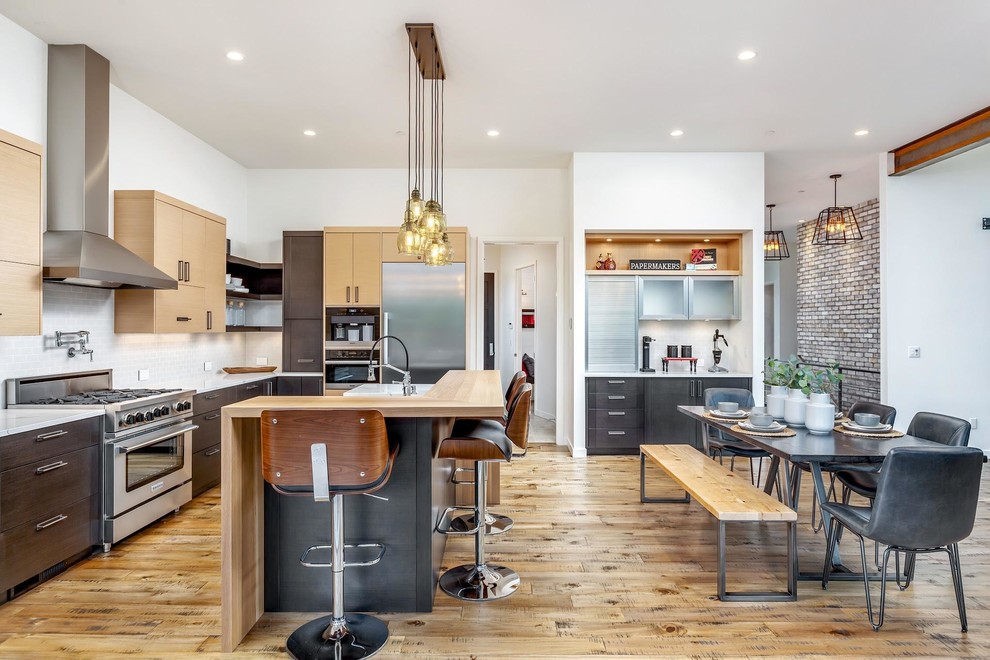 Example of a mid-sized trendy l-shaped medium tone wood floor and brown floor eat-in kitchen design in Portland with a farmhouse sink, flat-panel cabinets, dark wood cabinets, quartz countertops, white backsplash, subway tile backsplash, stainless steel appliances, an island and white countertops