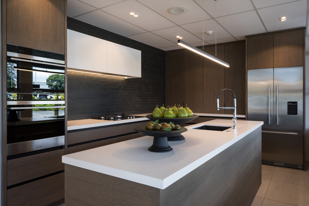 Medium sized contemporary l-shaped kitchen in Auckland with a single-bowl sink, medium wood cabinets, engineered stone countertops, black splashback, stone tiled splashback, stainless steel appliances, porcelain flooring, an island, white floors and white worktops.