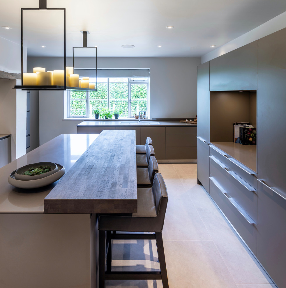 Photo of a large contemporary l-shaped kitchen pantry in Cheshire with a belfast sink, flat-panel cabinets, grey cabinets, engineered stone countertops, white splashback, brick splashback, stainless steel appliances, ceramic flooring, an island, white floors and grey worktops.
