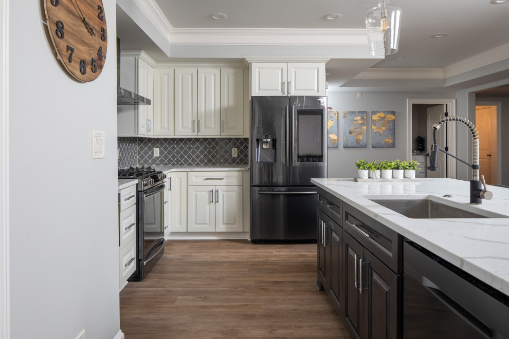 Klassisk inredning av ett mellanstort vit vitt kök, med en undermonterad diskho, luckor med upphöjd panel, beige skåp, bänkskiva i kvarts, grått stänkskydd, stänkskydd i glaskakel, svarta vitvaror, laminatgolv, en köksö och beiget golv