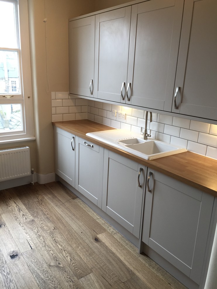 Inspiration for a small victorian medium tone wood floor eat-in kitchen remodel in London with a double-bowl sink, shaker cabinets, gray cabinets, wood countertops, white backsplash, subway tile backsplash, paneled appliances and no island