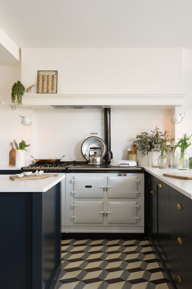 Bild på ett vintage vit vitt l-kök, med skåp i shakerstil, svarta skåp, vitt stänkskydd, stänkskydd i tunnelbanekakel, vita vitvaror, en köksö och flerfärgat golv