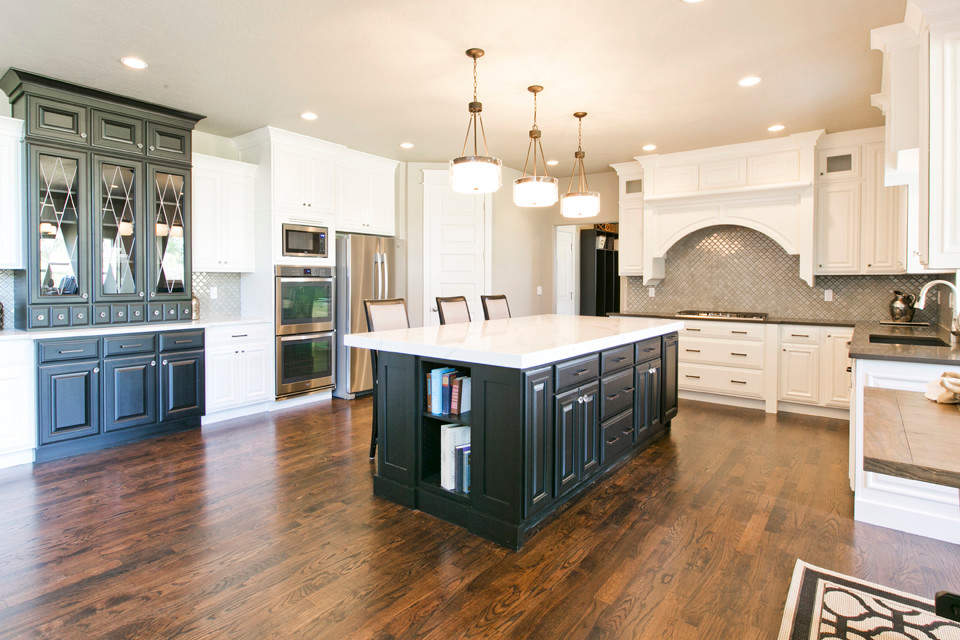 Large traditional l-shaped kitchen/diner in Salt Lake City with a submerged sink, recessed-panel cabinets, white cabinets, engineered stone countertops, metallic splashback, ceramic splashback, stainless steel appliances, medium hardwood flooring and an island.