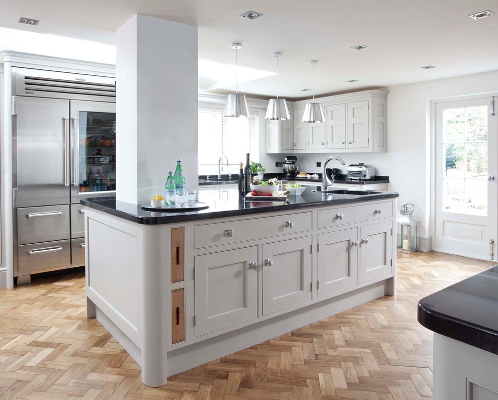 This is an example of a medium sized classic single-wall kitchen in Other with shaker cabinets, grey cabinets, granite worktops, grey splashback, metro tiled splashback, light hardwood flooring, an island and brown floors.