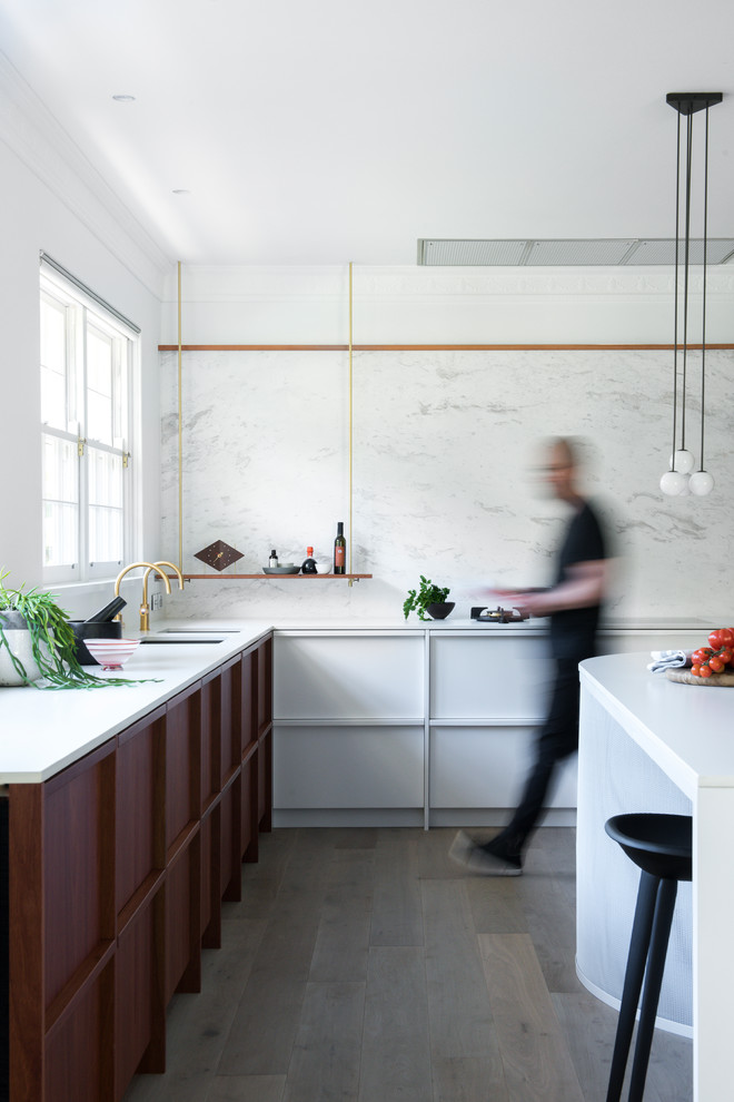 Inredning av ett modernt stort kök, med en undermonterad diskho, luckor med upphöjd panel, vita skåp, bänkskiva i kvarts, vitt stänkskydd, stänkskydd i marmor, svarta vitvaror, ljust trägolv och en köksö