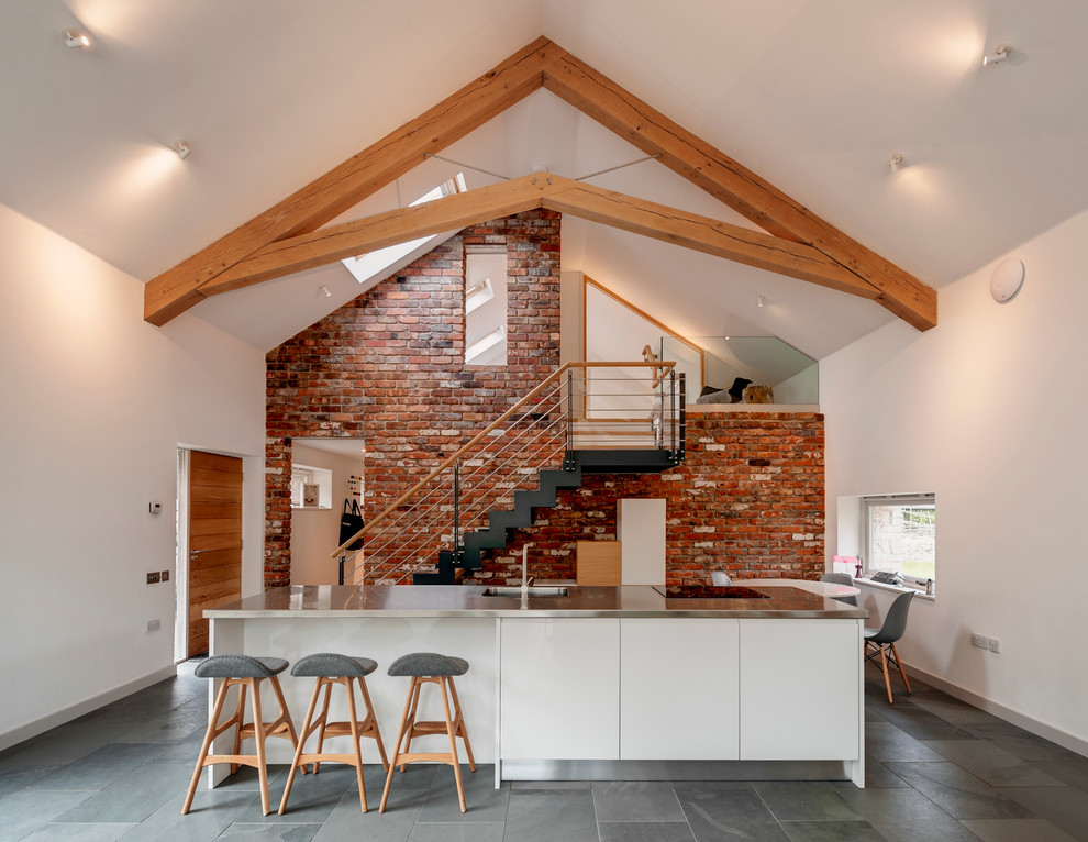 Moderne Wohnküche mit flächenbündigen Schrankfronten, weißen Schränken, Edelstahl-Arbeitsplatte, Schieferboden und Kücheninsel in Devon
