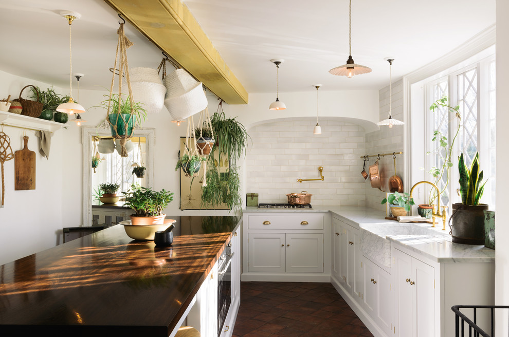 Design ideas for a vintage kitchen/diner in Other with a belfast sink, shaker cabinets, white cabinets, marble worktops, white splashback, metro tiled splashback, integrated appliances, terracotta flooring, an island and brown floors.