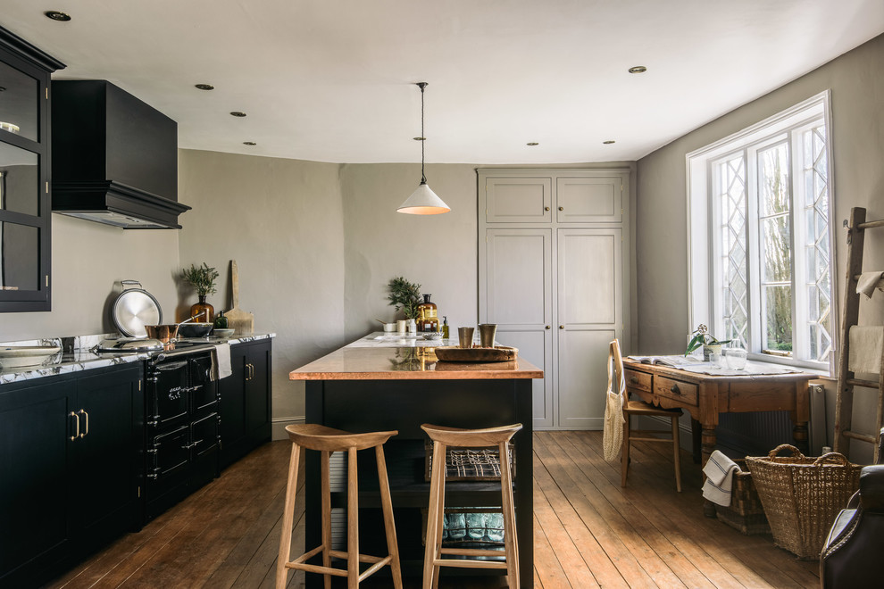 Example of a mid-sized cottage single-wall medium tone wood floor open concept kitchen design in Other with an integrated sink, shaker cabinets, black cabinets, copper countertops, gray backsplash, black appliances and an island