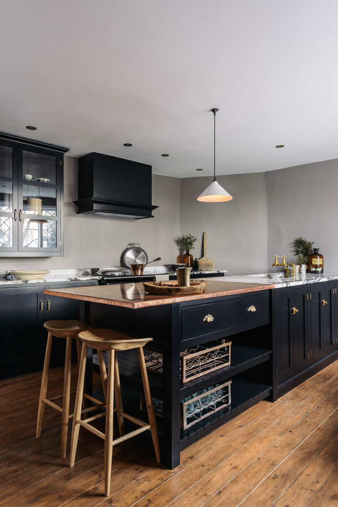 Inspiration pour une cuisine ouverte linéaire rustique de taille moyenne avec un évier intégré, un placard à porte shaker, des portes de placard noires, un plan de travail en cuivre, une crédence grise, un électroménager noir, un sol en bois brun et îlot.