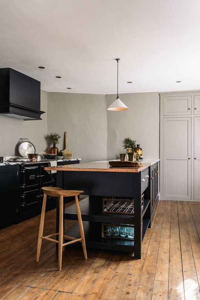 Bild på ett mellanstort lantligt linjärt kök med öppen planlösning, med en integrerad diskho, skåp i shakerstil, svarta skåp, bänkskiva i akrylsten, grått stänkskydd, svarta vitvaror, mellanmörkt trägolv och en köksö
