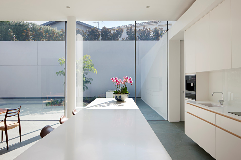 Moderne Wohnküche mit Unterbauwaschbecken, weißen Schränken, Mineralwerkstoff-Arbeitsplatte, Küchenrückwand in Weiß, Glasrückwand, Elektrogeräten mit Frontblende, Schieferboden, grünem Boden und weißer Arbeitsplatte in Melbourne