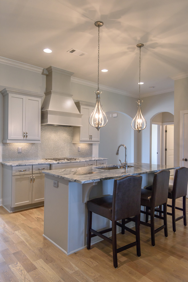 Photo of a large classic l-shaped open plan kitchen in Atlanta with a submerged sink, shaker cabinets, grey cabinets, granite worktops, grey splashback, glass sheet splashback, stainless steel appliances, medium hardwood flooring, an island and beige floors.