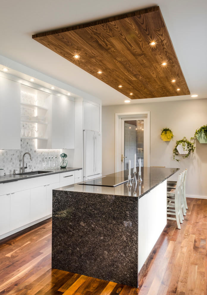 Example of a mid-sized minimalist galley medium tone wood floor open concept kitchen design in Cleveland with an undermount sink, flat-panel cabinets, white cabinets, granite countertops, white backsplash, stone tile backsplash, white appliances and an island