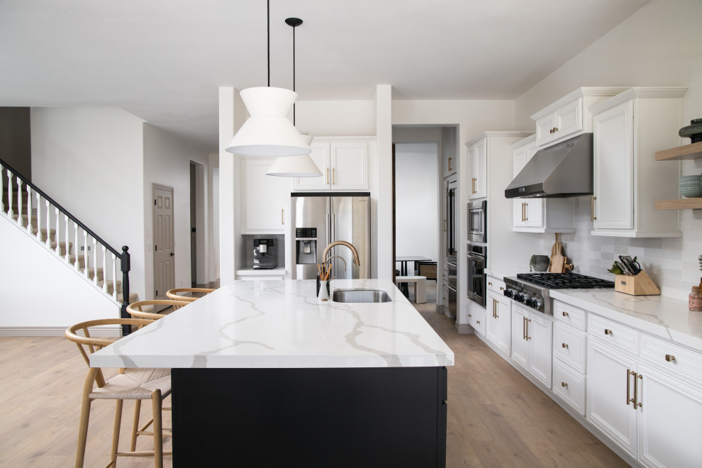 Idéer för ett minimalistiskt vit l-kök, med en undermonterad diskho, luckor med infälld panel, vita skåp, vitt stänkskydd, rostfria vitvaror, mellanmörkt trägolv, en köksö och brunt golv