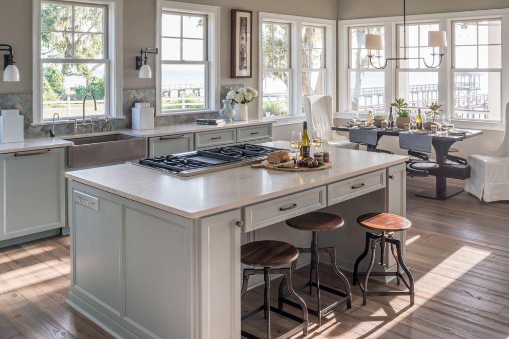 Diseño de cocina comedor marinera con fregadero sobremueble, armarios con paneles empotrados, puertas de armario azules, salpicadero metalizado, suelo de madera clara y una isla