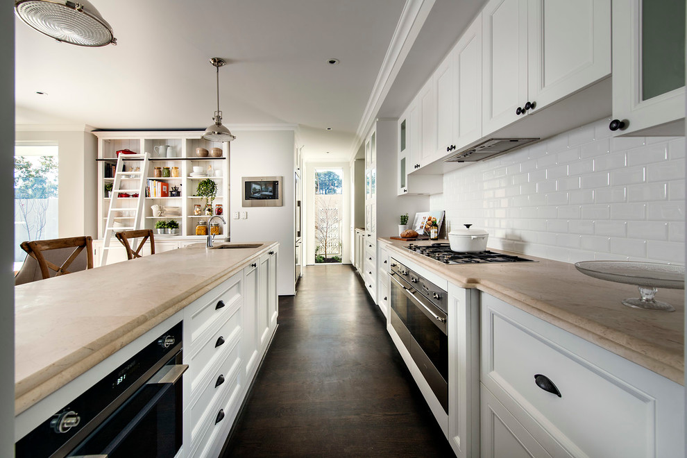 Klassisk inredning av ett kök, med en undermonterad diskho, luckor med infälld panel, vita skåp, vitt stänkskydd, stänkskydd i tunnelbanekakel, rostfria vitvaror, mörkt trägolv och en köksö