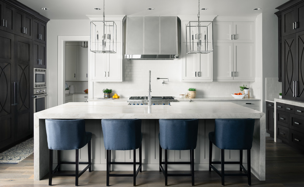 Imagen de cocina clásica renovada con armarios estilo shaker, puertas de armario blancas, salpicadero blanco, salpicadero de azulejos tipo metro, electrodomésticos de acero inoxidable, suelo de madera oscura, una isla, suelo marrón y encimeras grises