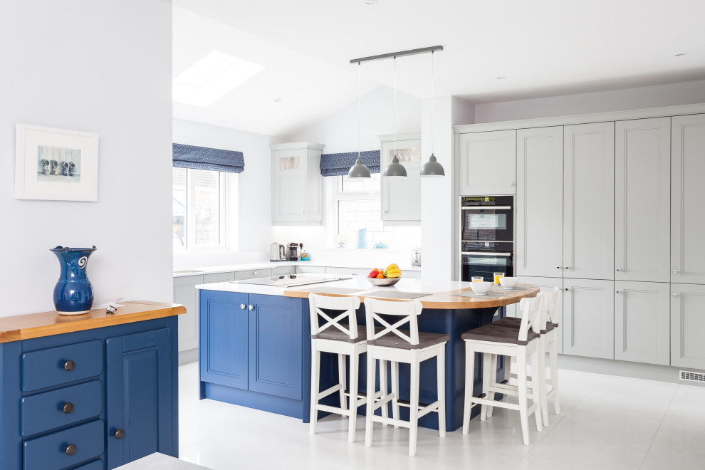 This is an example of a large traditional l-shaped kitchen in Cork with recessed-panel cabinets, grey cabinets, black appliances, an island, grey floors and white worktops.