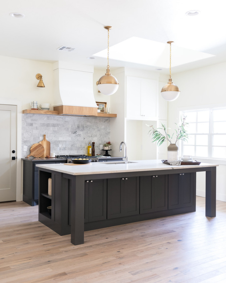 Photo of a large farmhouse l-shaped open plan kitchen in Oklahoma City with a submerged sink, shaker cabinets, black cabinets, quartz worktops, grey splashback, marble splashback, stainless steel appliances, light hardwood flooring, an island, brown floors and grey worktops.