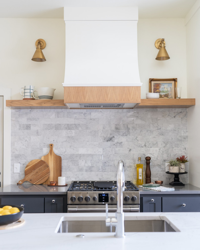 Lantlig inredning av ett stort grå grått kök, med en undermonterad diskho, skåp i shakerstil, svarta skåp, bänkskiva i kvartsit, grått stänkskydd, stänkskydd i marmor, rostfria vitvaror, ljust trägolv, en köksö och brunt golv