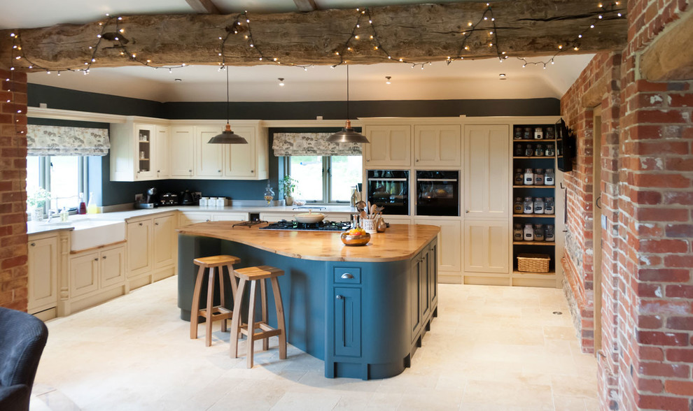 Large country l-shaped kitchen in Other with a belfast sink, recessed-panel cabinets, wood worktops, blue splashback, stainless steel appliances, an island and beige floors.