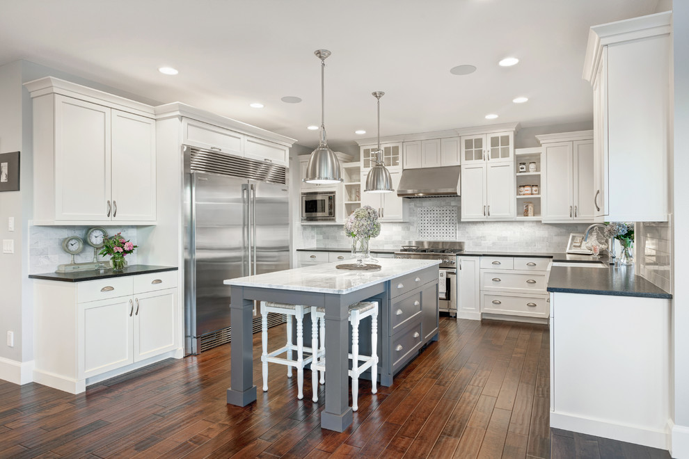 Kitchen - traditional u-shaped kitchen idea in Vancouver with a farmhouse sink, recessed-panel cabinets, white cabinets, marble countertops, white backsplash, stainless steel appliances and stone tile backsplash