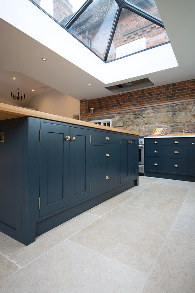 Mittelgroße Landhaus Küche mit Schrankfronten im Shaker-Stil, blauen Schränken, Kalkstein, Kücheninsel und beigem Boden in Sonstige