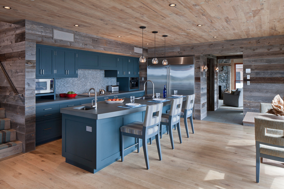 Photo of a rustic galley open plan kitchen in Boston with shaker cabinets, blue cabinets, grey splashback, stone slab splashback, stainless steel appliances and light hardwood flooring.