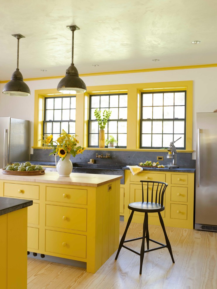 Photo of a farmhouse kitchen in New York with a belfast sink, beaded cabinets, yellow cabinets, grey splashback, stainless steel appliances, light hardwood flooring and multiple islands.