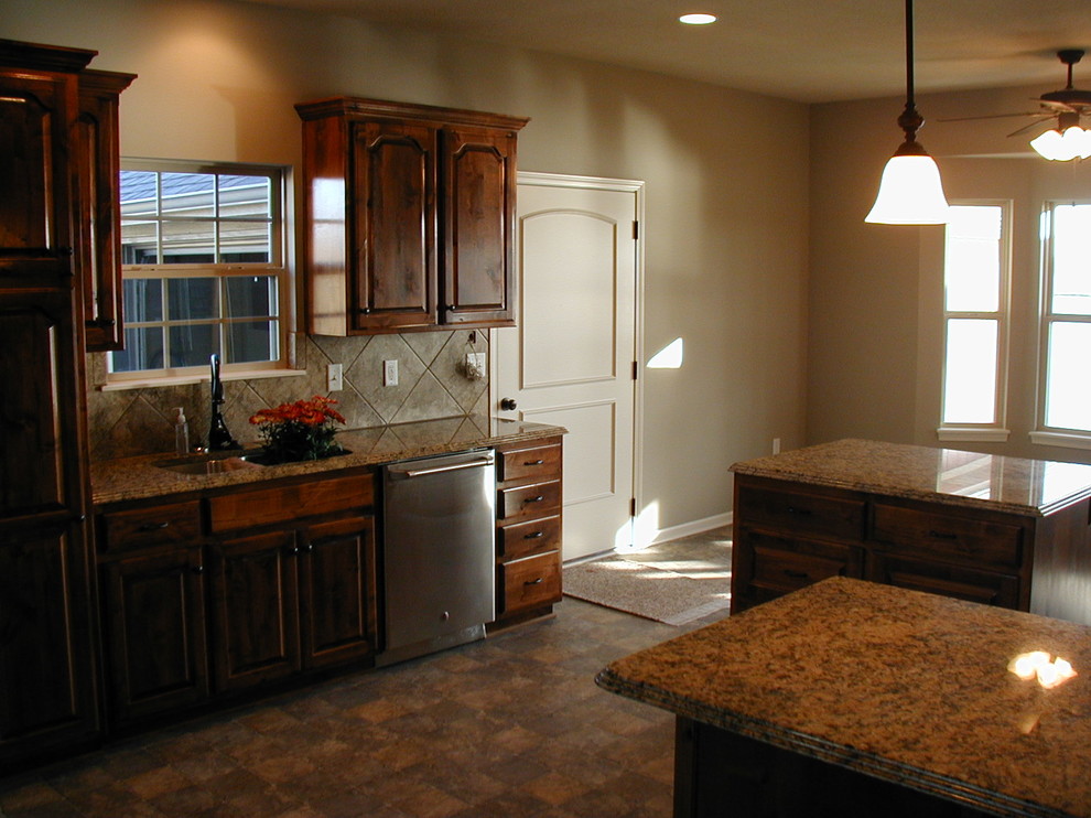 Ejemplo de cocina rural con fregadero bajoencimera, armarios con paneles con relieve, puertas de armario de madera en tonos medios, encimera de granito, salpicadero beige, salpicadero de azulejos de cerámica, electrodomésticos de acero inoxidable, suelo de baldosas de cerámica y dos o más islas