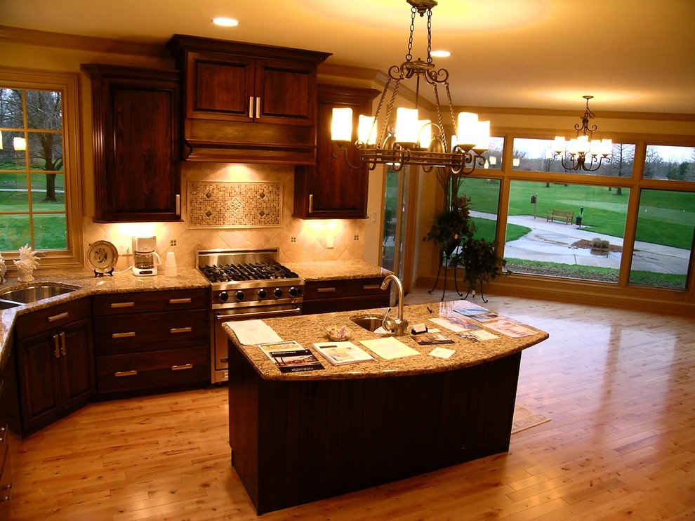 Inspiration for a large traditional u-shaped kitchen in Chicago with a double-bowl sink, raised-panel cabinets, dark wood cabinets, granite worktops, beige splashback, ceramic splashback, stainless steel appliances, light hardwood flooring, an island, beige floors and beige worktops.