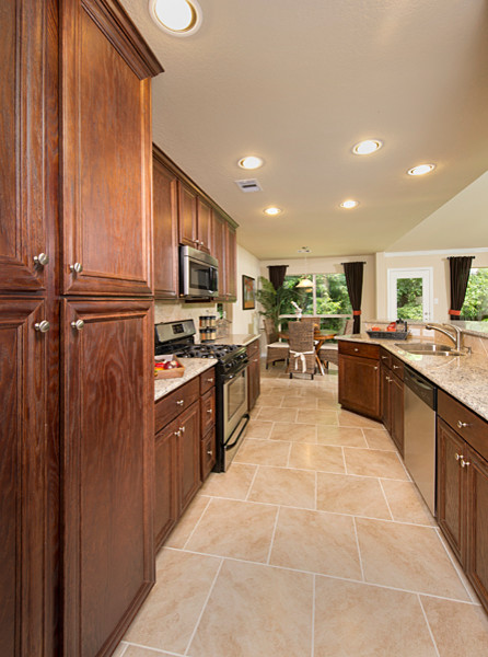 Mid-sized elegant galley porcelain tile and beige floor eat-in kitchen photo in Houston with an undermount sink, beaded inset cabinets, dark wood cabinets, granite countertops, beige backsplash, limestone backsplash, stainless steel appliances, a peninsula and beige countertops
