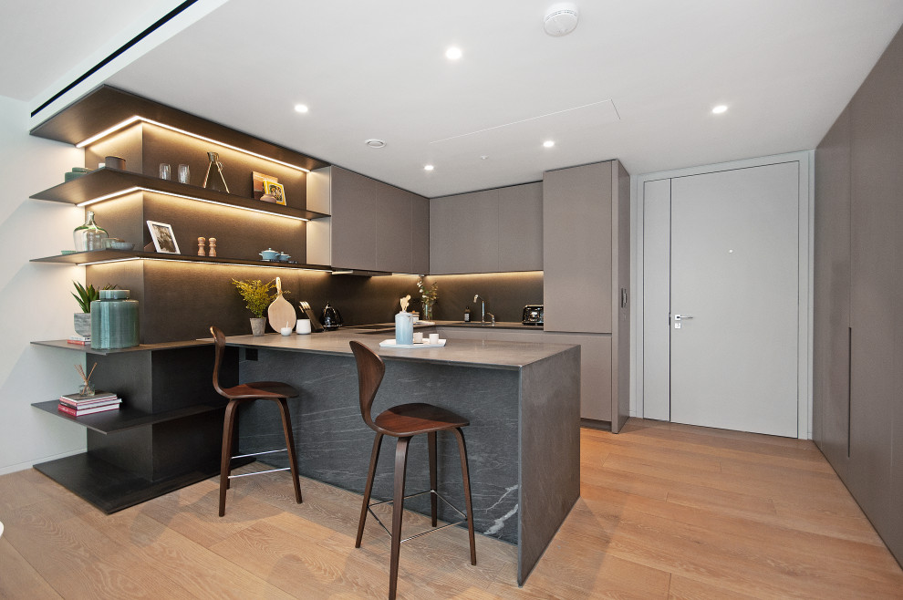 Design ideas for a contemporary u-shaped kitchen in London with a submerged sink, flat-panel cabinets, grey cabinets, integrated appliances, light hardwood flooring, a breakfast bar, beige floors and grey worktops.