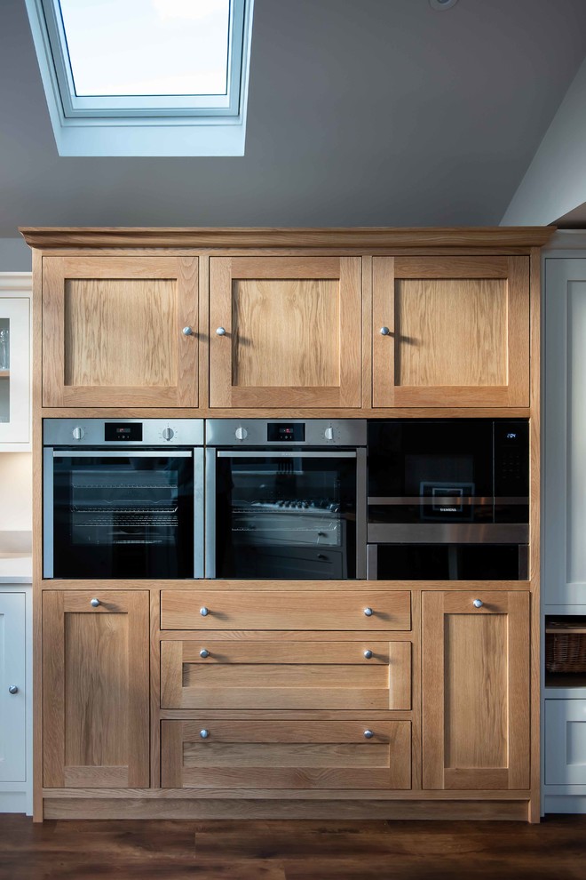 Foto på ett stort funkis grå kök, med en dubbel diskho, skåp i shakerstil, vita skåp, bänkskiva i kvartsit, grått stänkskydd, mellanmörkt trägolv och en halv köksö