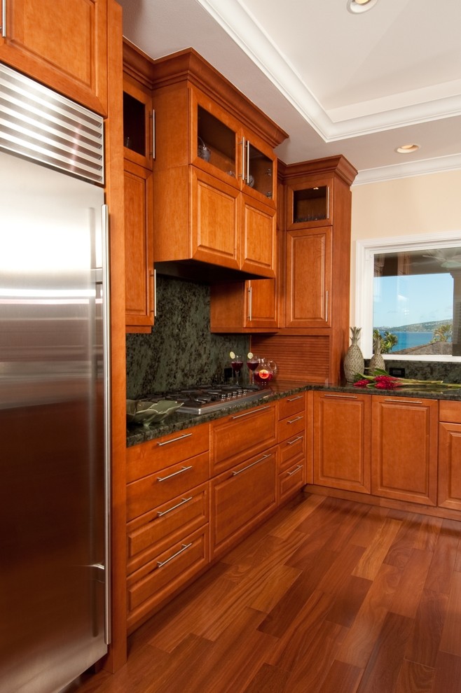 Moderne Wohnküche mit Küchengeräten aus Edelstahl, profilierten Schrankfronten, hellbraunen Holzschränken, Küchenrückwand in Grün und Rückwand aus Stein in Hawaii