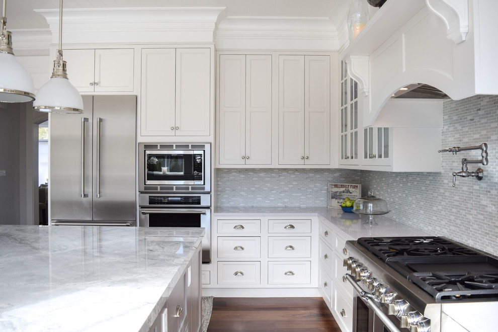 Bild på ett stort maritimt kök, med en rustik diskho, luckor med infälld panel, vita skåp, bänkskiva i kvartsit, grått stänkskydd, stänkskydd i marmor, rostfria vitvaror, mörkt trägolv och en köksö
