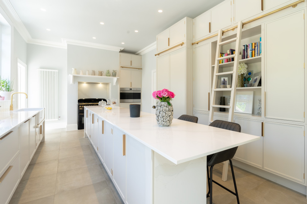 This is an example of a contemporary u-shaped enclosed kitchen in London with a belfast sink, recessed-panel cabinets, white cabinets, white splashback, integrated appliances, an island, beige floors and white worktops.