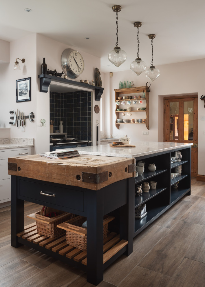 Design ideas for a farmhouse kitchen in Other with flat-panel cabinets, white cabinets, black appliances, an island, brown floors and white worktops.