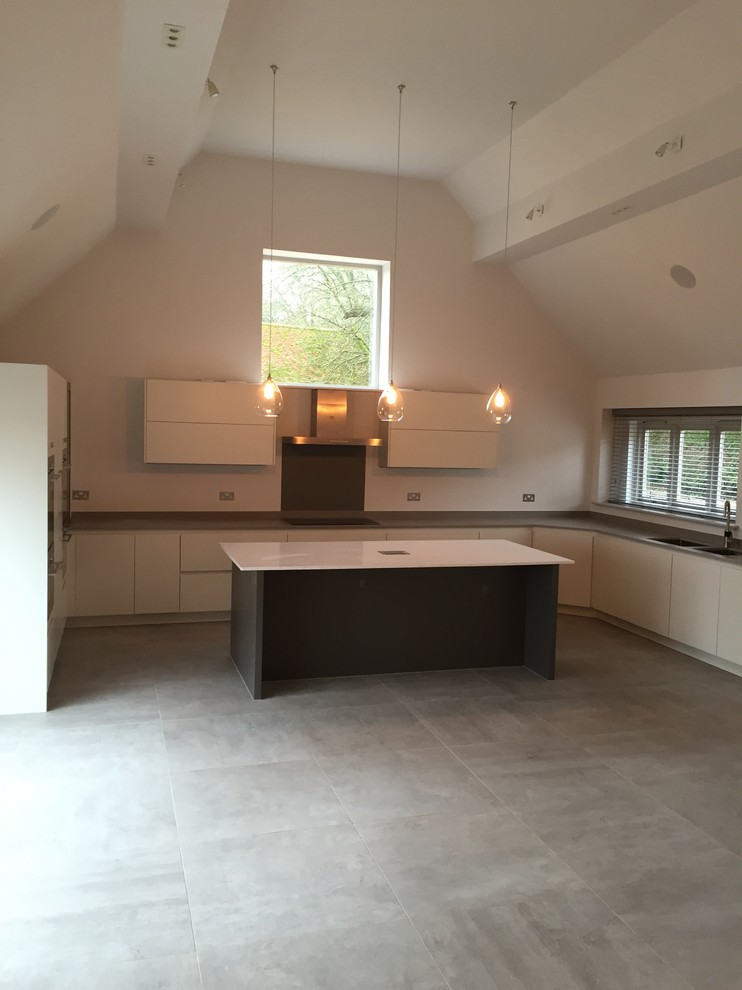 Inspiration for an expansive contemporary u-shaped kitchen/diner in Wiltshire with a double-bowl sink, flat-panel cabinets, white cabinets, grey splashback, glass sheet splashback, black appliances, porcelain flooring, an island and engineered stone countertops.