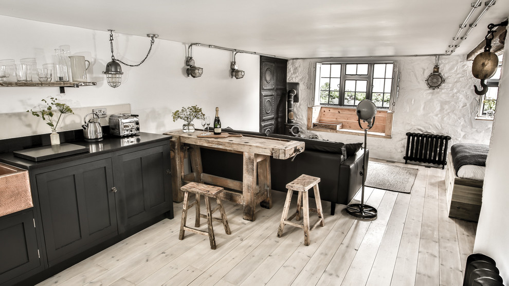 Bild på ett litet industriellt kök, med en rustik diskho, skåp i shakerstil, svarta skåp, granitbänkskiva, vitt stänkskydd, stänkskydd i cementkakel, integrerade vitvaror, ljust trägolv och en halv köksö