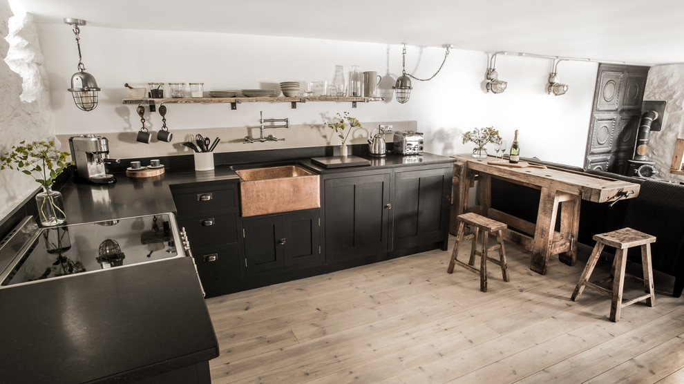 Foto på ett litet industriellt kök, med en rustik diskho, skåp i shakerstil, svarta skåp, granitbänkskiva, vitt stänkskydd, stänkskydd i cementkakel, integrerade vitvaror, ljust trägolv och en halv köksö
