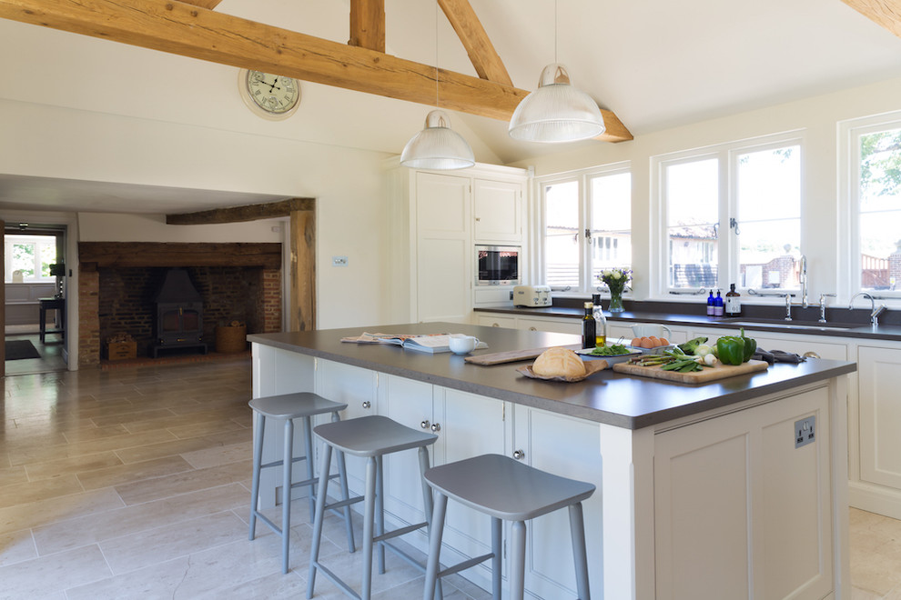 Photo of a large traditional l-shaped open plan kitchen in Essex with white cabinets, metallic splashback, mirror splashback, stainless steel appliances, limestone flooring, an island, a submerged sink and recessed-panel cabinets.
