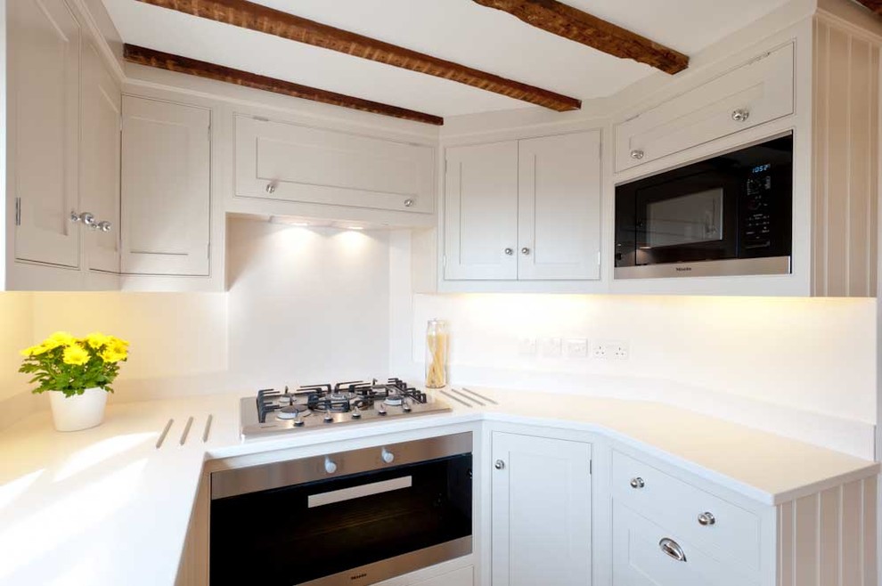 Small classic u-shaped enclosed kitchen in London with a belfast sink, shaker cabinets, white cabinets, stainless steel appliances and medium hardwood flooring.
