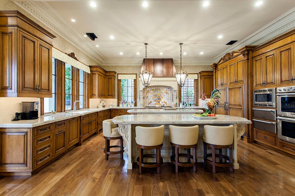 Example of a huge tuscan u-shaped medium tone wood floor eat-in kitchen design in Orange County with a farmhouse sink, recessed-panel cabinets, medium tone wood cabinets, limestone countertops, multicolored backsplash, cement tile backsplash, stainless steel appliances and two islands